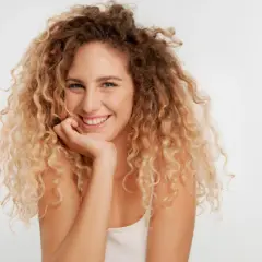 Uśmiechnięta kobieta z burzą blond loków, które tworzą piękne **skręty włosów**.