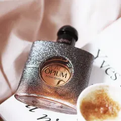 Błyszcząca butelka Black Opium od YSL, z nutą **opium floral shock**, obok filiżanki kawy i książki.