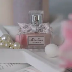 Elegancka butelka Miss Dior 100ml z kokardką, otoczona perłami i delikatnymi, białymi kulkami.