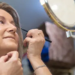 Kobieta po 50. roku życia poprawia makijaż, delikatnie podkreślając oczy. Widać subtelne zmiany skórne na twarzy, które dodają jej charakteru.