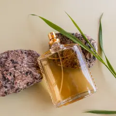 Szklana butelka z płynem, otoczona kamieniami i trawą. Przywołuje wspomnienie kultowych perfum lat 90 męskich.