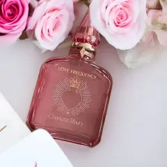Różowe róże otaczają flakonik perfum Charlotte Tilbury Love Frequency.
