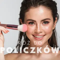 Uśmiechnięta kobieta z pędzlem do różu na policzku. Dowiedz się, jak nakładać róż dla naturalnego efektu.