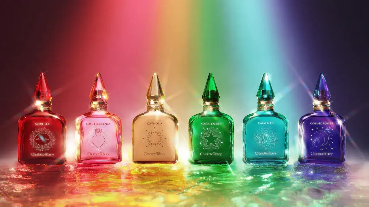 Sześć kolorowych buteleczek perfum Charlotte Tilbury, każda z innym symbolem i nazwą, lśni na tle tęczy.
