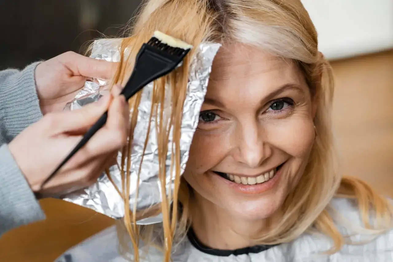 Kobieta po 40. z uśmiechem na twarzy, jej blond włosy są farbowane. Jasny kolor włosów dodaje jej uroku i odmładza.