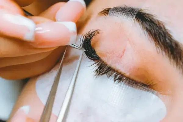 Precyzyjne przedłużanie rzęs 2-3d. Stylistka z perfekcyjnym manicurem dokłada kolejne kępki, tworząc efekt wow.
